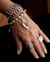 Layered stainless steel bracelets featuring a chunky chain, ball chain with a leaf pendant, and a hammered bangle.