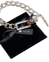 Leather and silver-plated metal necklace and bracelet set, featuring a chunky chain and belt buckle design, presented on a black suede pouch.