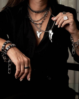 Person wearing multiple necklaces, bracelets, and rings with a blurred background