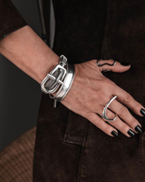 Close-up of a hand wearing multiple silver bracelets and rings on a dark background