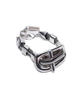 A silver-toned metal bracelet featuring a large, sculptural buckle-like centerpiece with textured mesh details and a spring-ring clasp, shown on a plain white background.