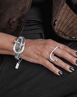 Close-up of a hand wearing a silver bracelet and ring, with a brown coat in the background.