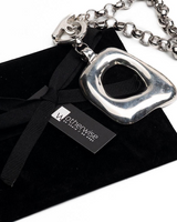 Silver necklace with a black ribbon on a black stand, branded 'OtherWise'.
