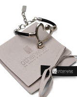 Black leather bracelet with a silver heart centerpiece, presented on a suede gift pouch from Otherwise Jewelry.