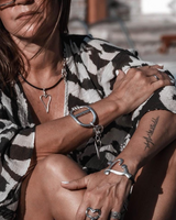 Silver heart necklace set worn on a model, featuring a black leather necklace with a heart pendant and two adjustable silver-tone bracelets.