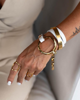 Close-up of a hand wearing gold bracelets and rings with a neutral background