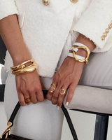 Close-up of hands wearing gold bracelets and rings with a handbag in the foreground.