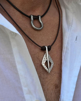 Close-up of a silver pendant on a black cord worn by a person with a white shirt.
