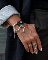 Bold black leather bracelet with oversized silver horseshoe shackle, worn with stacked silver adjustable rings on a hand.