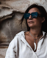 Woman wearing sunglasses and a light-colored shirt against a textured stone wall.