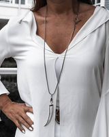 Person wearing a white blouse with ruffled sleeves and a long necklace.