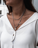Close-up of a person wearing a white blouse and layered necklaces with a blurred background.