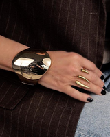 Chunky honey gold geometric cuff bracelet worn on wrist, featuring a smooth, reflective finish against a brown jacket.