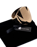 Geometric cuff bracelet in shiny honey gold, featuring a wide design and spring coil opening, placed on a black velvet pouch.