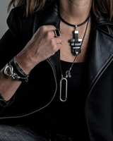 Black leather and metal bar choker necklace layered with additional necklaces, worn by a model in a black leather jacket.