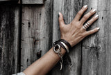 Funky silver-plated metal ring worn on the index finger, paired with layered leather bracelets against a wooden background.