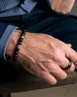Close-up of a person's hand wearing a bracelet and ring, with a blurred background.