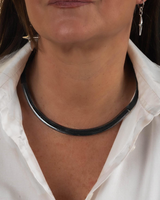 Layered gunmetal choker necklace featuring curved metal tube design, worn over a white collared shirt.