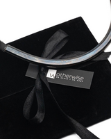 Gunmetal choker with a sleek metal tube design, resting on a black velvet pouch with a ribbon tie.