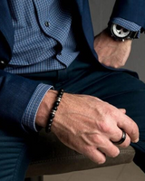 Person wearing a blue suit with a watch and bracelet, sitting on a chair.