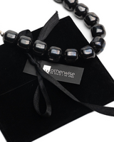 Edgy black gemstone choker with smooth, chunky beads resting on a black suede pouch, featuring a ribbon tie and brand tag.
