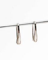 Silver earrings hanging from a rod on a white background