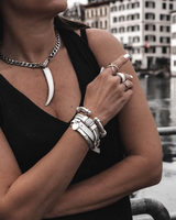 Leather cuff bracelet with silver zamak accents, stacked with multiple bracelets and worn on a model's wrist.
