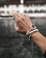 Hammered silver metal bangle wrapped with leather strap on a wrist, showcasing an adjustable and stacking style.