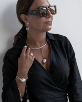 Woman wearing a black outfit with jewelry against a plain background