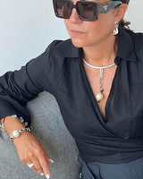 Woman wearing a black outfit with sunglasses and jewelry against a light background