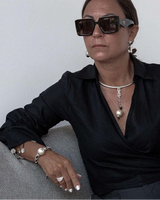Woman wearing sunglasses and a black outfit sitting on a gray couch against a white wall.