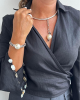 Person wearing a dark gray blouse with pearl embellishments, a necklace, and bracelet against a white background.