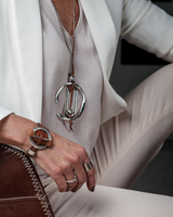 Person wearing a white outfit with a necklace and bracelet, sitting on a dark surface.