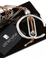 Silver and brown leather necklace on a black box with 'otherwise jewelry' card.