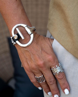 Chunky black leather cuff bracelet with a large silver horsebit centerpiece, worn on a wrist with multiple silver rings.