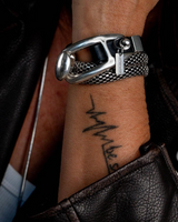Close-up of a wrist wearing a silver bracelet with a clasp design, featuring a tattoo on the skin.