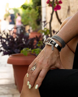 Person's wrist with multiple bracelets and a ring, sitting outdoors.