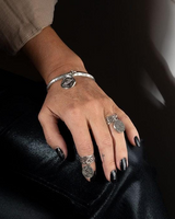 Hand wearing silver rings and a bracelet on a dark surface