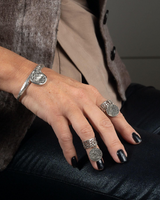 Close-up of a hand wearing multiple silver rings with dark nail polish, sitting on a surface.