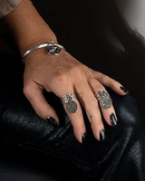 Hand with multiple rings and a bracelet on a dark surface