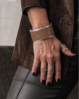 Person wearing a brown coat and gray pants with a gold bracelet and ring.