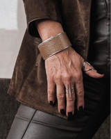 Person wearing a brown textured bracelet and ring on a blurred background