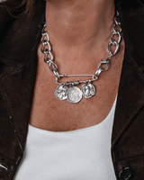 Silver chain bracelet with charms on a person wearing a brown jacket and white top.