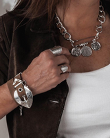 Person wearing silver jewelry including a necklace, bracelet, and rings on a neutral background