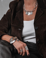 Person wearing a brown jacket with a white top, black pants, and silver jewelry.