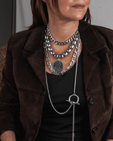 Layered necklace set featuring stainless steel chains and dark gemstone beads, worn with a dark jacket and top.