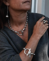 Person wearing silver jewelry including a necklace, bracelet, and ring.