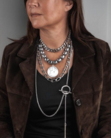 Bold layered necklace set combining stainless steel chains and dark gemstones, worn over a black top and brown jacket.