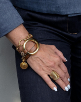 Hand wearing a gold bracelet and ring on a neutral background