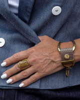 A close-up of a person's hand wearing a textured taupe leather bracelet with gold-toned hardware and a matching ring, styled with a blue denim blazer.
